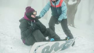 Person checks on a snowboarder sitting down on the mountain