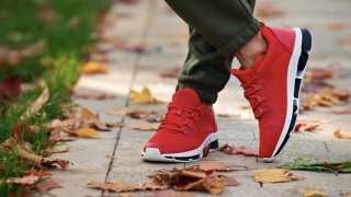Close up of two red sneakers on a sidewalk in the fall. 
