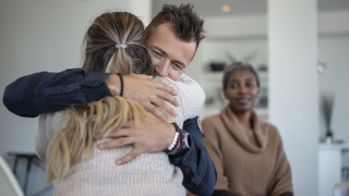 A young caucasian male is hugging a female in a group therapy class. 