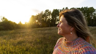 A woman enjoying nature while standing in a field while the sun is setting..