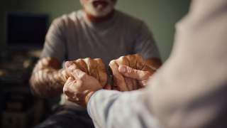 Close up of a provider and senior patient holding hands in hospital.