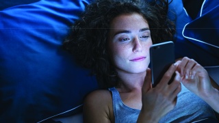Adult woman using smartphone while in bed at night.