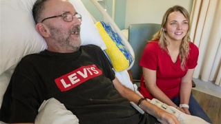 A visitor sits next to a patient laying in bed.