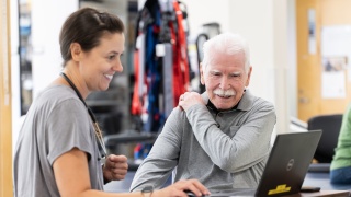 A medical provider speaks to a patient who is holding their shoulder.
