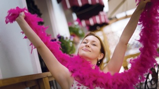 A woman puts her arms in the air holding a pink boa.
