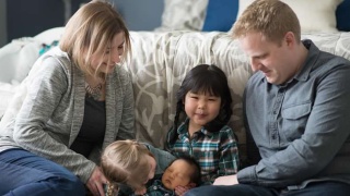 A couple sits on a sofa with their three young children.