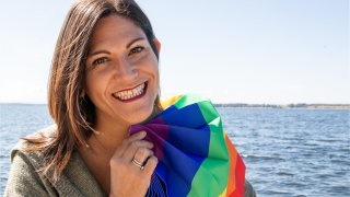 Portrait of Dani Frusco holding a rainbow flag.