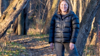 Gabby Makatura poses for a photo while standing outside in a stand of trees.