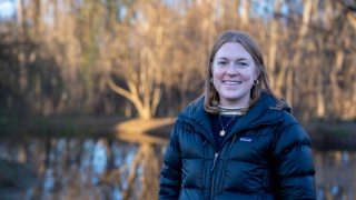 Gabby Makatura poses for a photo while standing outside in a stand of trees.
