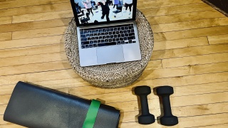 A Steps to Wellness participant uses a laptop, yoga mat and hand weights at home.