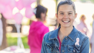 A young girl smiles wearing a breast cancer ribbon.