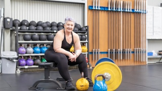 Adult woman sits on weight bench in gym during weight lifting session.