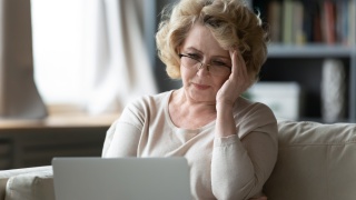 Adult woman holds forehead in frustration while using a computer.