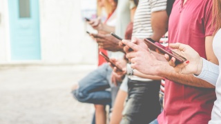 People stand in a line while holding and using their smartphones.