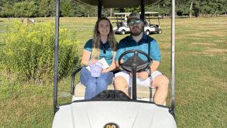 Two volunteers sit on a golf cart.