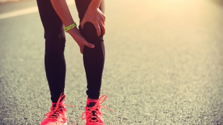 Stock photo of a runner holding their knee on a roadway.