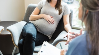 Stock photo of a pregnant woman sitting and talking to a doctor.
