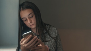 Young girl looks at cell phone in a dark room.