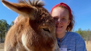 A girl poses with a donkey.