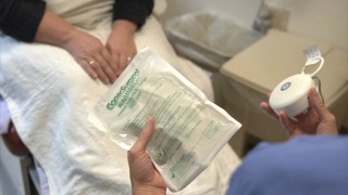 Provider holding an instant heat pack and small speaker device beside a patient seated on an exam table.