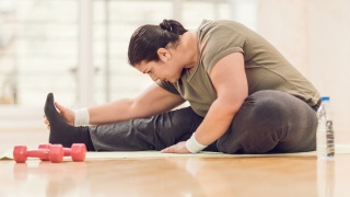 A woman stretches next to weights.