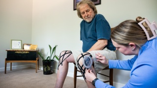 Home health physical therapist adjusts patient's leg brace.