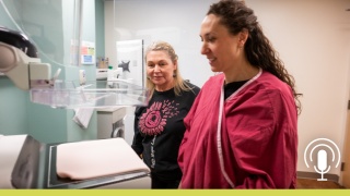 Patient and healthcare professional standing beside a mammography machine in a breast imaging exam room.