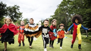 Children wearing Halloween costumes hold hands and race on a lawn.