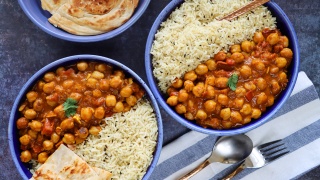Bowls of curried chickpeas, jasmine rice and naan sit a blue table. 
