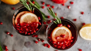 Two glasses of Pomegranate Citrus Mocktail sit on a table topped with lemon slices, rosemary and pomegranate seeds.