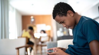 Teenage boy sits with his head bent down and looks at a phone screen.