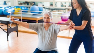 A woman uses stretch bands with the help of a physical therapist during cardiac rehab.
