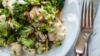 Broccoli cauliflower salad sits in a bowl next to a fork and knife.