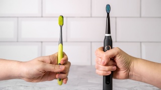 Two hands hold a regular toothbrush and an electric toothbrush.