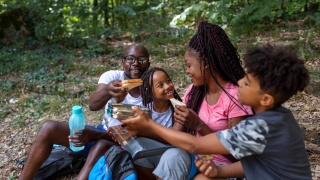 A family eats sandwiches on a camping trip hike.