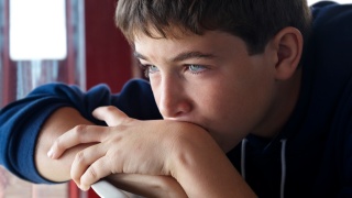 A young boy looks sad while thinking with his head resting on his hands.