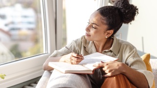 A woman sits near a window writing in her journal.