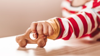 A young child plays with a wooden toy car.