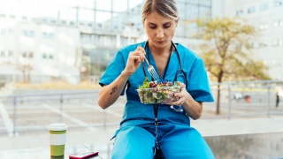 A female health care worker sits and eats a salad at the hospital.