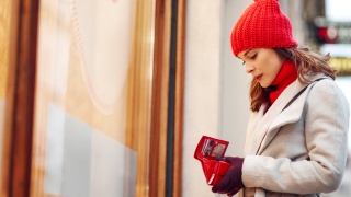 A woman wearing a winter hat checks her wallet while shopping.