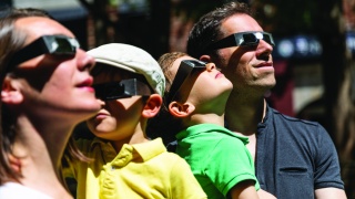 Family with adult and children wear eclipse glasses to safely watch eclipse