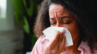 Black woman with allergies sneezes into tissue