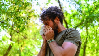 Man with allergies sneezing or blowing nose into tissue outdoors