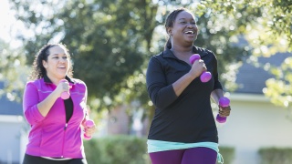 Two women walk for exercise with weights in hands.