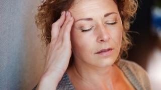 Older woman with hand to head in migraine pain.