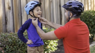 A father attaches bike helmet for sports safety. 