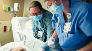 Nurses stand over a bedside.