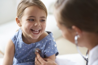 A medical provider listens to a smiling pediatric patient's heart beat. 