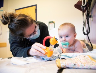 A medical provider holds a toy in front of a small baby. 