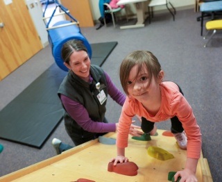 A pediatric rehab specialist helps a young patient climb a ramp.